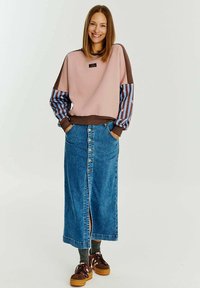 Ružová a hnedá mikina s pruhovanými rukávmi, v kombinácii s dlhou džínsovou sukňou s predným gombíkovým zapínaním. Hnedé a žlté tenisky.