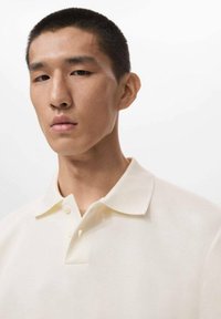 Polo-Shirt in hellem Cremefarbton, aus weichem Material, mit klassischem Kragen, Drei-Knopf-Leiste und glatter Textur.