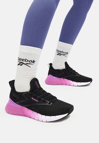 Pantofi de alergare negri cu accente roz, superior din plasă texturată și o talpă căptușită cu un design distinct segmentat. Sosete albe cu logo vizibile.