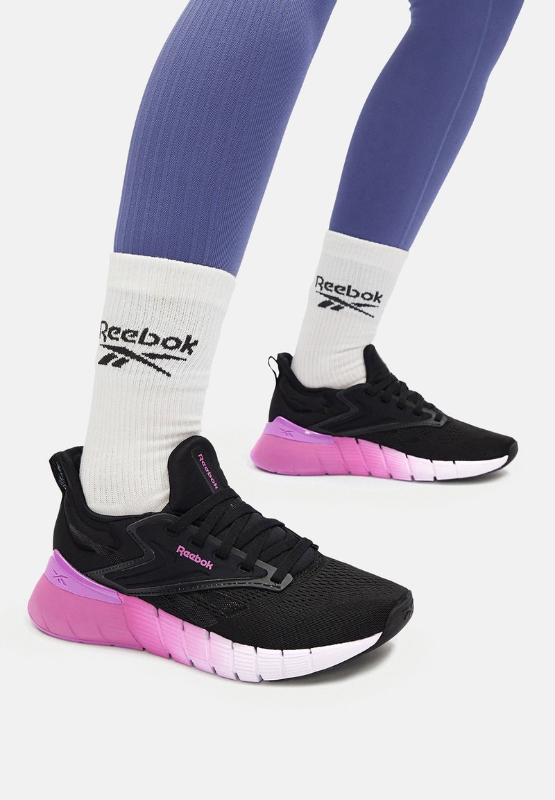 Pantofi de alergare negri cu accente roz, superior din plasă texturată și o talpă căptușit�ă cu un design distinct segmentat. Sosete albe cu logo vizibile.