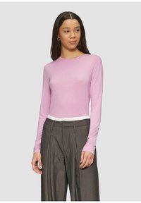 Lange mouwen roze top van zachte stof, met een ronde halslijn en een witte accent aan de zoom, gecombineerd met grijsgestreepte broek.