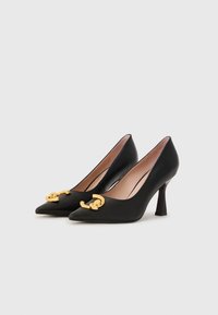 Escarpins en cuir noir à bout pointu avec un accent en chaîne dorée à l'avant, présentant un talon modéré et une texture lisse.