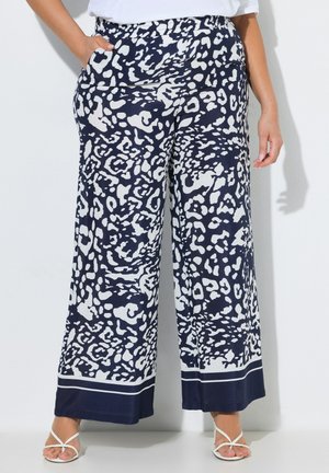 Bukser med vide ben med marineblåt og hvidt abstrakt dyreprint, båret med hvide rem-sandaler og en hvid top.