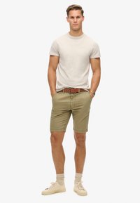 Beige T-shirt, olijfgroene shorts met zakken, bruine riem, crèmekleurige sneakers en lichtbruine sokken. Standaard pasvorm, casual ontwerp.