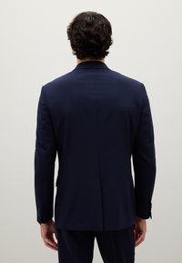 Giacca di abito blu navy, con un solo spacchetto sul retro, vestibilità sagomata, tessuto liscio, dettagli minimi e bottoni coordinati ai polsini.