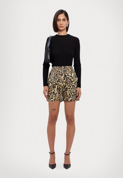 Top de manga larga negro con textura acanalada, combinado con pantalones cortos de leopardo en tonos beige y negro. Modelo lleva tacones con pulsera de tobillo y sostiene un pequeño bolso negro.