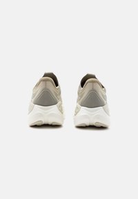 Ζευγάρι αθλητικών παπουτσιών σε μπεζ και λευκό χρώμα, εμφανιζόμενα από πίσω, με παχιά σόλα και θηλιά στο τακούνι, σε λευκό φόντο.