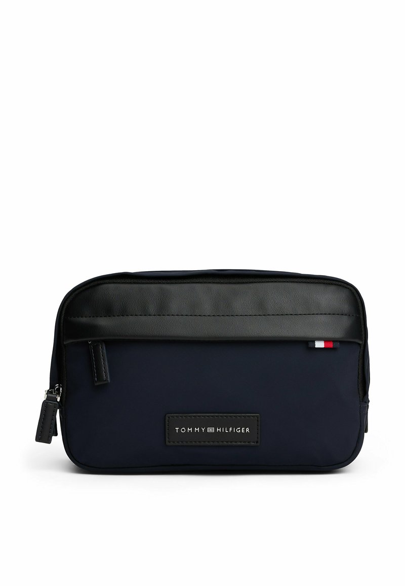 Beauty case in tessuto blu navy con parte superiore in pelle nera, chiusura con zip e una toppa con logo. Presenta una piccola striscia di accento rossa, bianca e blu.