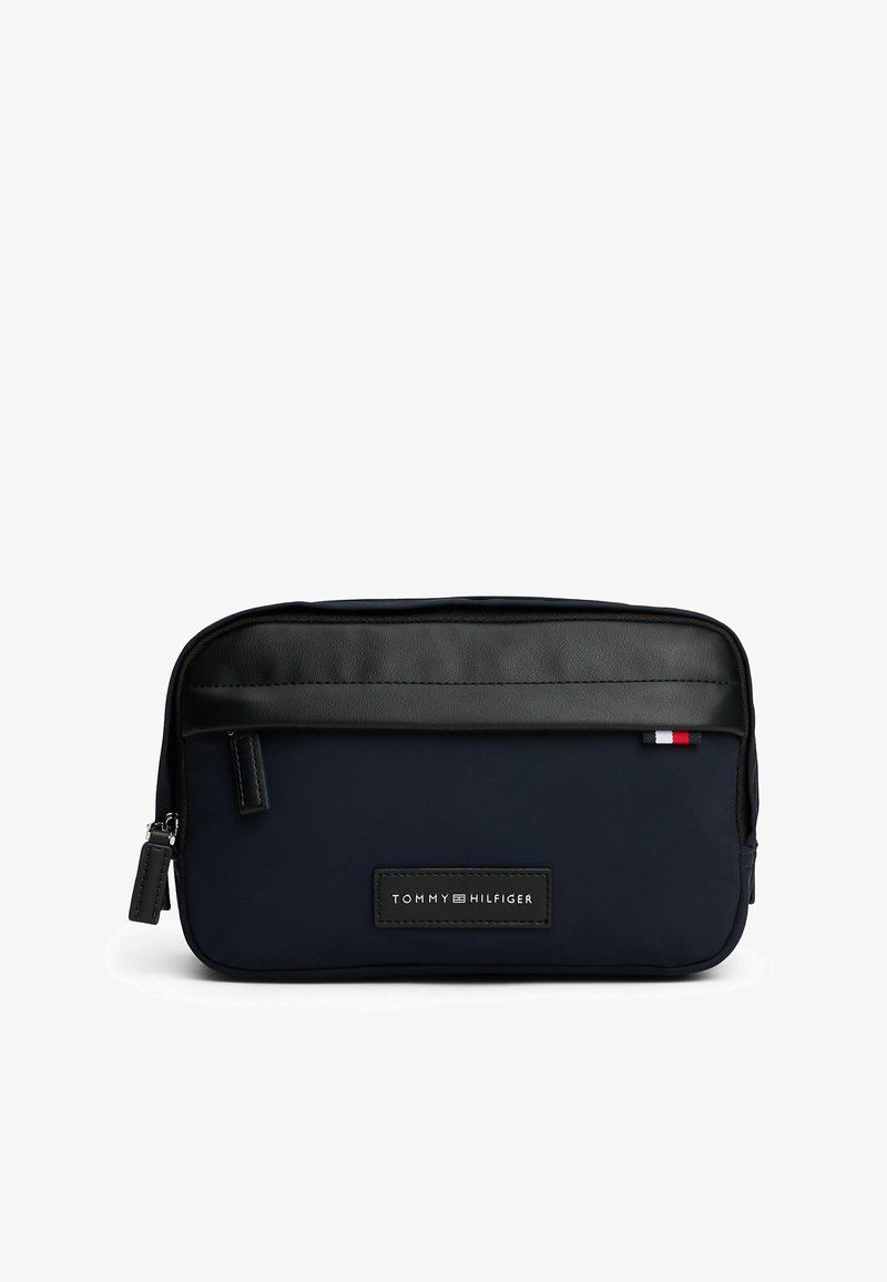 Marineblauwe toilettas van stof met een zwarte leren top, ritssluiting en een logo patch. Voorzien van een kleine accentstreep in rood, wit en blauw.