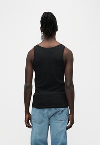 Μαύρο βαμβακερό αμάνικο τοπ με στρογγυλή λαιμόκοψη, στενή εφαρμογή και χωρίς ορατά λογότυπα, συνδυασμένο με ανοιχτό μπλε τζιν παντελόνι.