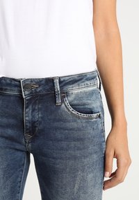 Bleka blå denimjeans med en klassisk femfickdesign, knappstängning och synliga sömdetaljer, i kombination med en vit topp.