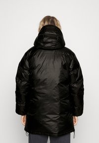 Veste noire matelassée avec capuche, dotée d'une texture brillante et lisse, ainsi qu'un cordon de serrage à l'ourlet pour un ajustement réglable.