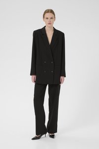 Černý pruhovaný dvouřadý blazer s klopovými límci, doplněný o odpovídající kalhoty. Lesklé střevíce na špičce dokončují celkový vzhled.