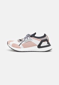 Baskets de sport rose clair avec un dessus en maille texturée, accents blancs, support de talon arrière noir et détails gris. Équipées d'un système de laçage.