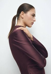 Vestido de satén color granate con silueta entallada. Mangas largas con textura suave, llevado por una modelo posando de perfil contra un fondo neutro.