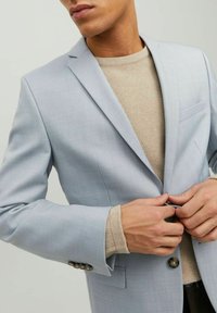 Giacca di completo azzurro chiaro con rever a pera e chiusura a tre bottoni. Tessuto liscio, taschino sul petto singolo e maniche con dettagli decorativi.