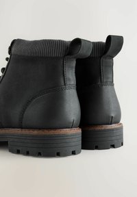 Zwarte enkelboots met een gladde leren afwerking, een gestructureerde gebreide manchette en een robuuste rubberen zool met uitgesproken profiel en trek lussen.