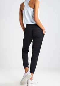 Svarta joggers i ett mjukt, texturerat tyg, med en elastisk midja och sidofickor, i kombination med en ljusblå linne och vita sneakers.