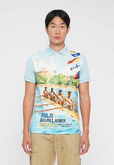 Férfi világoskék pólót visel, amelyen evezős csapat illusztráció, zászlók és a "Polo Ralph Lauren Regatta Race of Champions  Sept 08-67" szöveg látható.