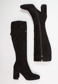 Botas de ante negras hasta la rodilla con un alto tacón cuadrado, que cuentan con un cierre de cremallera lateral y un detalle de cordones ajustables en la parte superior.