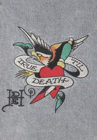 Broderad design med en färgglad fågel med vingar, ett rött hjärta och en banner som läser "SANN TILL DÖDEN" på grått tyg.