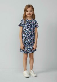 Bloemenjurk met korte mouwen, donkerblauwe achtergrond, kleurrijke bloemenprint, losse pasvorm, ronde halslijn, gecombineerd met witte sneakers.