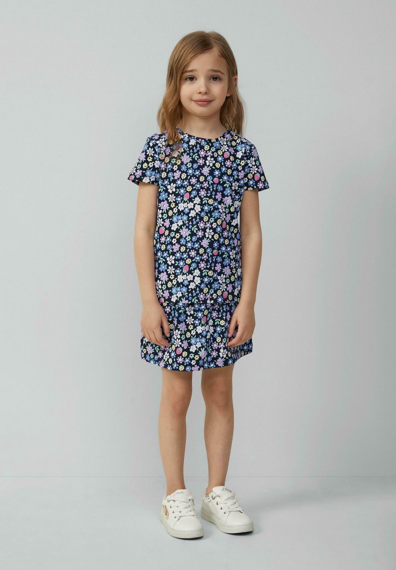 Bloemenjurk met korte mouwen, donkerblauwe achtergrond, kleurrijke bloemenprint, losse pasvorm, ronde halslijn, gecombineerd met witte sneakers.