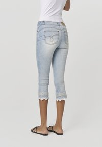 Jasno-niebieskie capri dżinsowe z koronkowym wykończeniem na nogawkach, z dwoma tylnymi kieszeniami i ozdobnym przeszyciem na kieszeniach.