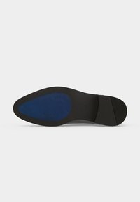 Semelle d'une chaussure formelle noire à bout pointu, avec une zone de grip bleue texturée à l'avant et une section de talon lisse.