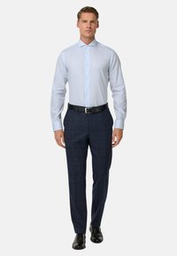 Světle modrá košile s ostrým límcem, zapínáním na knoflíky a dlouhými rukávy, doplněná o tmavé kostkované kalhoty a černé společenské boty.