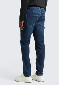 Jeans din denim albastru închis, cu croială dreaptă, buzunare spate cu clapete unghiulare și o textură ușor decolorată. Asortați cu adidași albi.