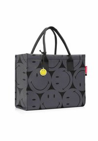 Borsa a tracolla grigia con un motivo che ripete volti sorridenti neri. Dotata di manici neri e un ciondolo sorridente giallo attaccato.