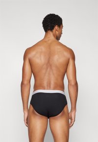 Schwarze enganliegende Shorts mit einem grauen elastischen Bund, glatter Textur und minimalistischem Design. Ansicht von hinten, die die Kontur und den Schnitt zeigt.