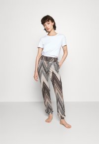 Vzorce, lahki hlače v rjavih in bež odtenkih z zigzag vzorcem; elastičen pas in manšete na gležnjih. Ujemajo se s preprosto belo majico.