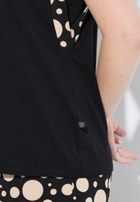 Zwarte t-shirt met beige stippenaccenten aan de zijkanten. Zachte stof, ontspannen pasvorm en klein logo label nabij de zoom.