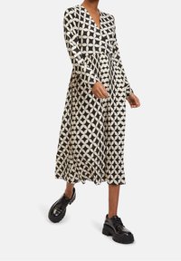 Dlouhé šaty v černé a bílé barvě se geometrickým vzorem. Volný silueta, výstřih do V a láskyplně stažený pas. V páru s černými platformovými botami.