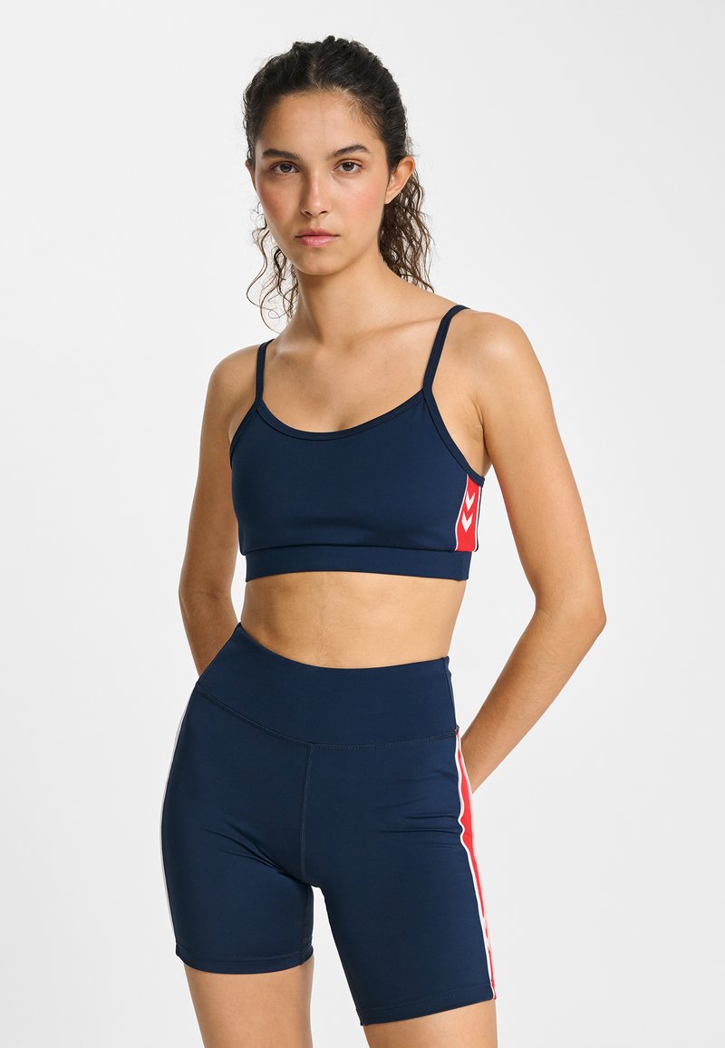 Brassière de sport bleu marine avec fines bretelles et accent rouge ; short taille haute assorti avec bandes latérales rouges ; tissu lisse et extensible.