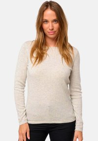 Pull long à manches longues gris clair avec un col rond, texture lisse et poignets côtelés, associé à un pantalon noir, design minimaliste.