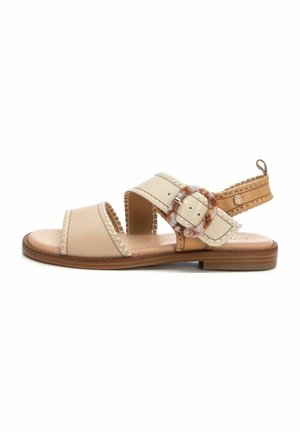 Sandalias de cuero beige con dos correas anchas, acentos trenzados y una hebilla decorativa. Suela plana con un acabado de madera natural.