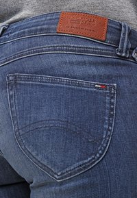 Jeans de mezclilla azul oscuro con un parche de logo de cuero, costuras curvas en los bolsillos traseros y un ajuste clásico con costuras visibles.