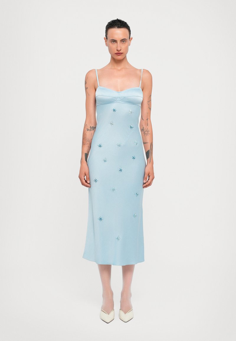 Vestido de satén azul claro con tirantes finos, adornado con lentejuelas en forma de estrella. Longitud hasta la mitad de la pantorrilla y silueta ajustada.