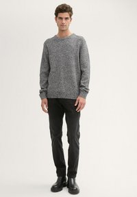 Grijze textuurgebreide trui met een ronde halslijn, gecombineerd met zwarte jeans en zwarte laarzen, getoond op een staande mannelijke model.