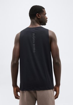 Muž otočený chrbtom, oblečený v čiernom tielku s vertikálnym nápisom "BJÖRN BORG" na chrbte, béžové šortky, neutrálne pozadie.