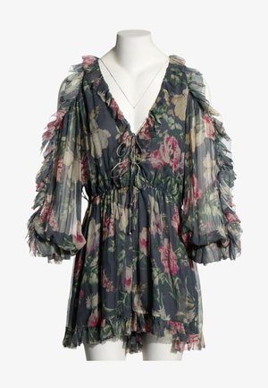 Robe romantique florale foncée en voile avec manches longues volantées, col en V et détail noué devant sur un mannequin blanc.