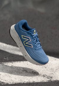 Scarpa da corsa blu con tomaia in rete, dettagli gialli e rosa, lacci rotondi, suola bianca ammortizzata e marchio "Fresh Foam" sul lato.