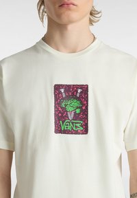Cremfarbene Baumwoll-T-Shirt mit einem zentralen Grafikdesign, das ein grünes Gehirn und Schrauben auf burgunderrot Hintergrund zeigt, mit der Marke "Vans" in grün.