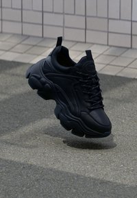 Svarta sneakers med en texturerad läderöverdel, tjock gummisula och snören, med en distinkt klumpig siluett och vadderad krage.