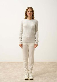 Pull en tricot gris clair avec côtes verticales, col rond et manches longues. Associé à un pantalon de jogging gris clair assorti et des baskets.
