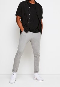 Korte mouwen zwart shirt met knopen, gecombineerd met grijze joggingbroeken en witte sneakers. Eenvoudig ontwerp, casual pasvorm, zachte textuur.