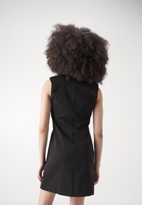 Svart ärmlös klänning med en figursydd silhuett, slät textur och subtila sömmar bak, som slutar ovanför knäet.